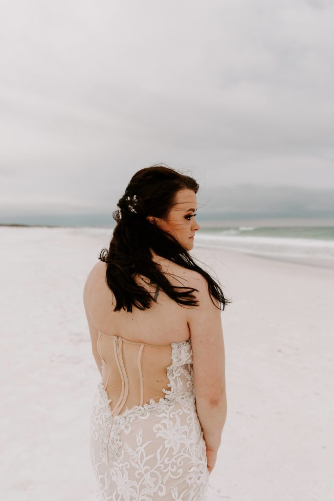 Woman looking off over her shoulder with the beach and ocean in front of her during her beach elopement