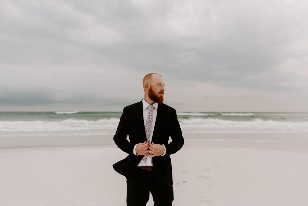 Man holding onto his blue suit jacket as he looks off to the side during his beach vow renewal