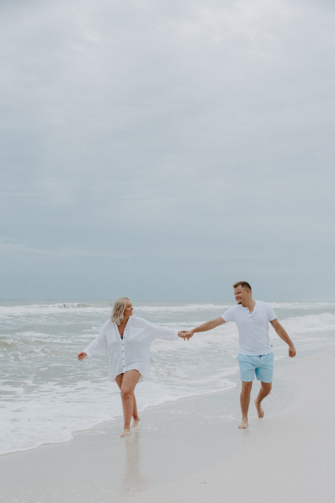 Couple holding hands out as far as they can as they walk along the ocean on the beach during their early morning couple photoshoot in Florida