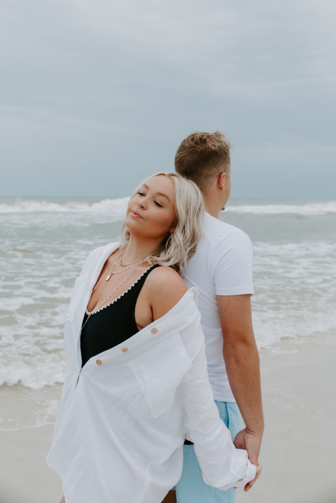Woman leaning against her partner as they hold hands during their beach engagement photos in Florida