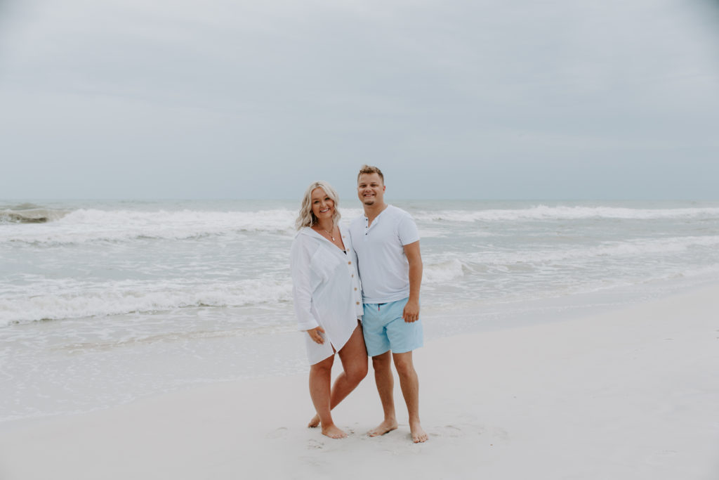 Couple smiling and standing with the gulf of mexico in the background during their beach engagement photos