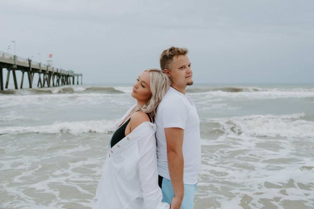 Couple standing back to back on the beach as they look off in the direction they are looking during their beach engagement photos in Florida