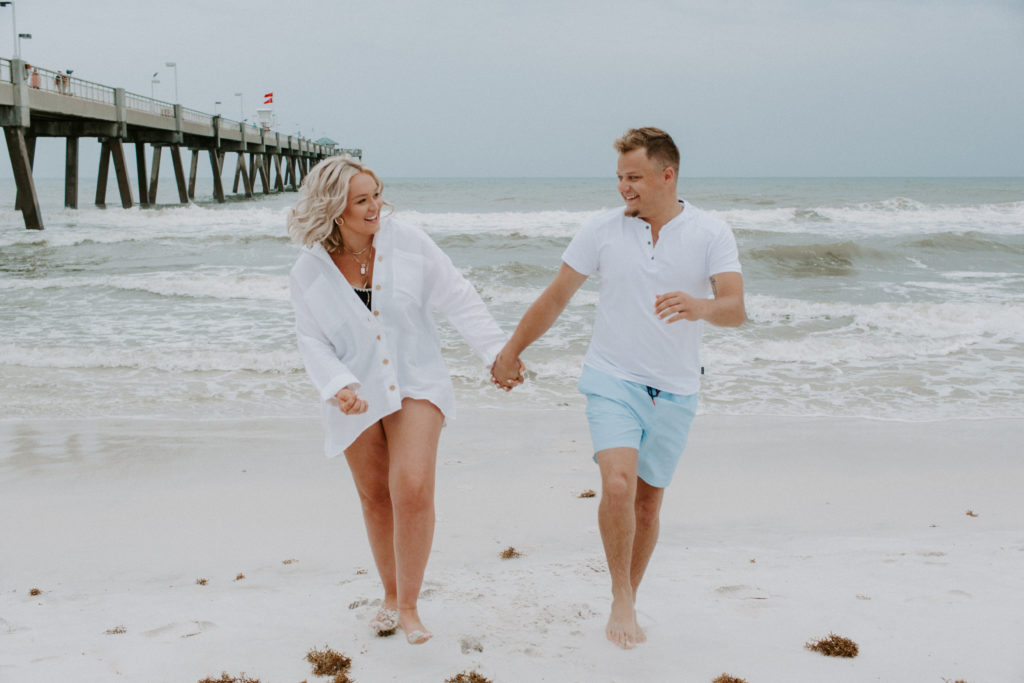 Couple holding hands and running along the beach as they look at each other and are smiling