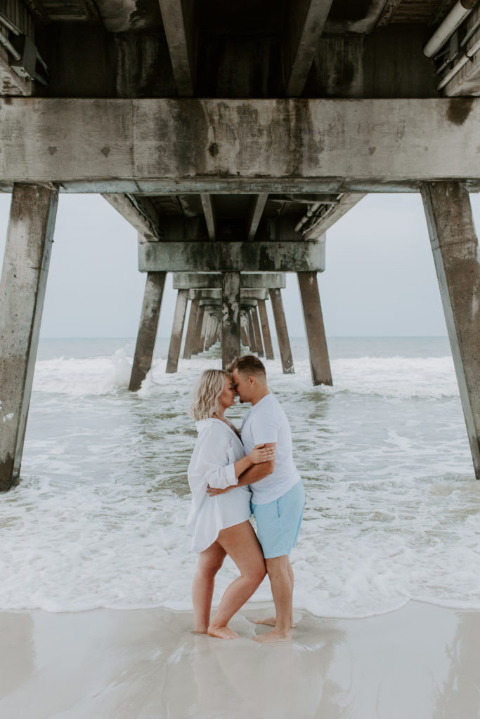 Couple standing under a pier with their foreheads resting on each others and their arms around each other