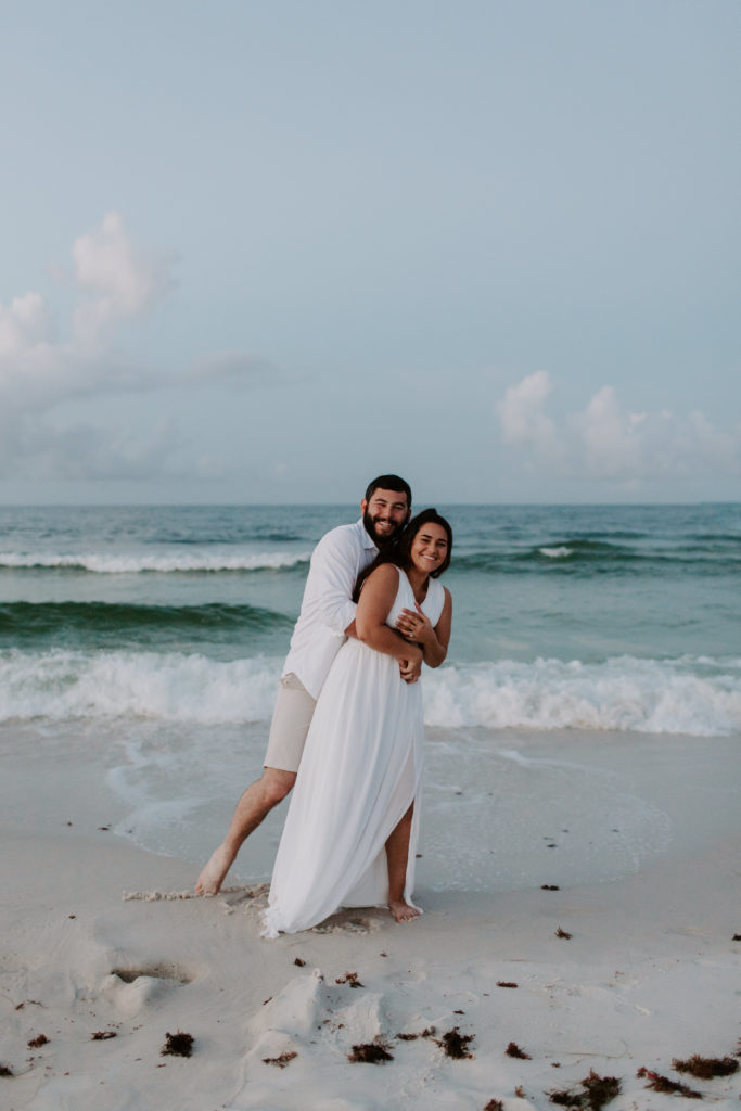 A man holding his partner from behind as she is laughing and smiling during their Destin, Florida engagement photos