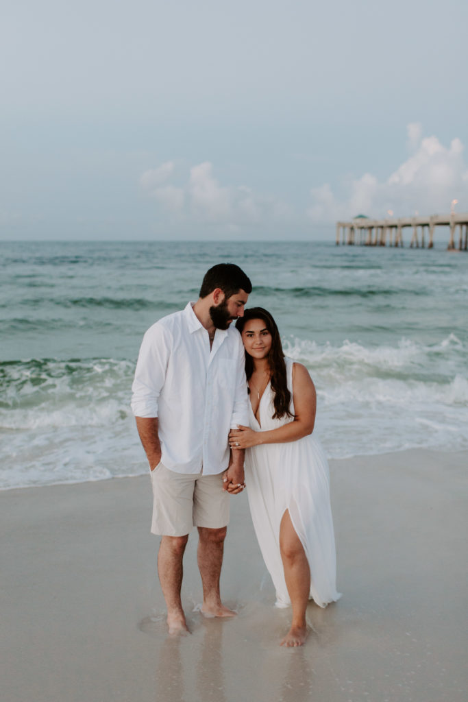 A man looking down at his partner as she looks off while holding onto his arm during their Florida engagement photos