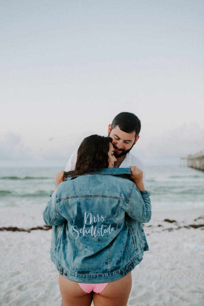 Woman popping the collar of her jean jacket that has her new last name written on it while her future husband looks down at her