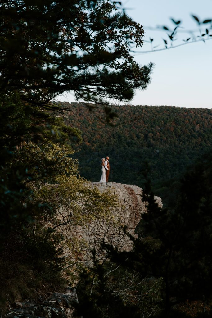 Woman standing with her arms wrapper around her partner looking off into the distance during their all day hiking elopement in Arkansas