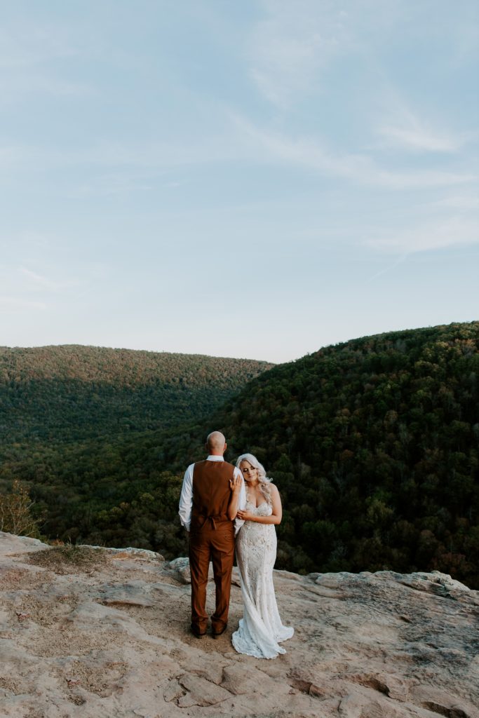Woman holding on to her partners arm with her eyes closed as he looks off at the rolling mountains during the sunset of their Arkansas elopement