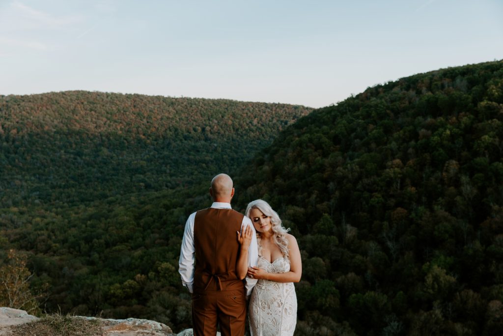 A woman hugging onto her partners arm as he faces the hills of Arkansas during their hiking elopement