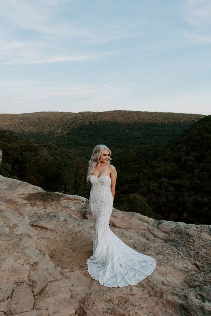 Woman standing on the edge of the cliffs holding her arms behind her back looking off into the distance in her wedding dress during her Arkansas elopement
