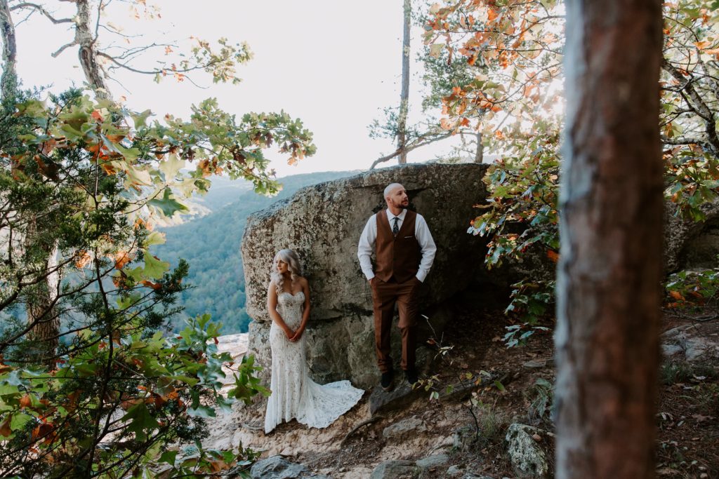 A couple standing a few feet apart while leaning up against a rock looking opposite directions of each other during their all day hiking elopement