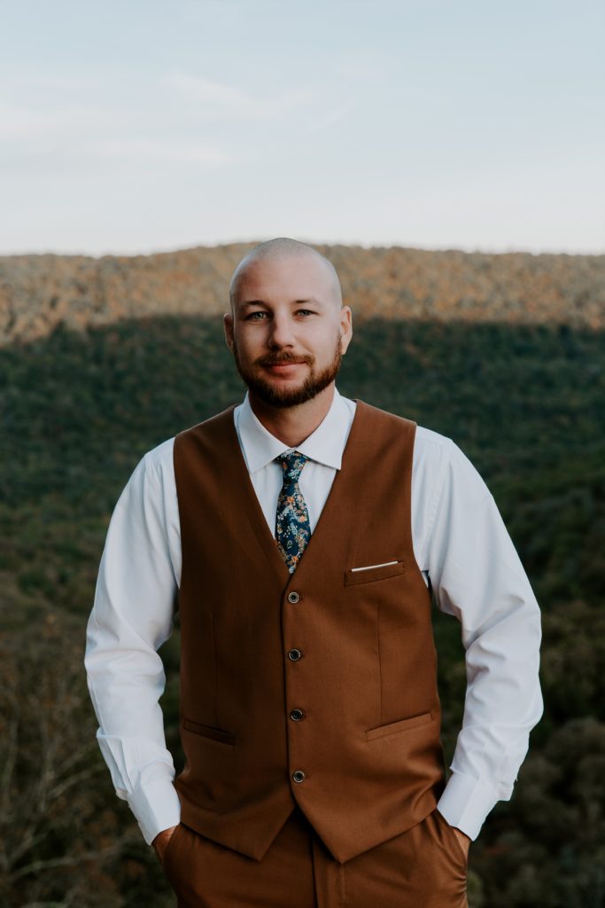 Groom standing with his hands in his pockets and a soft smile during the hiking part of their Arkansas elopement