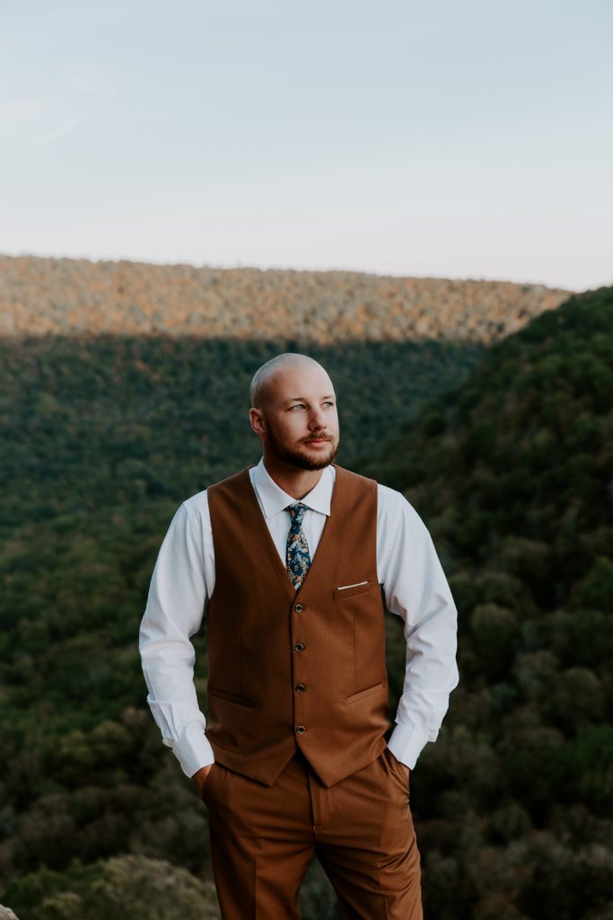 Man standing with his hands in his pockets looking off at the sunset during his Ozarks elopement