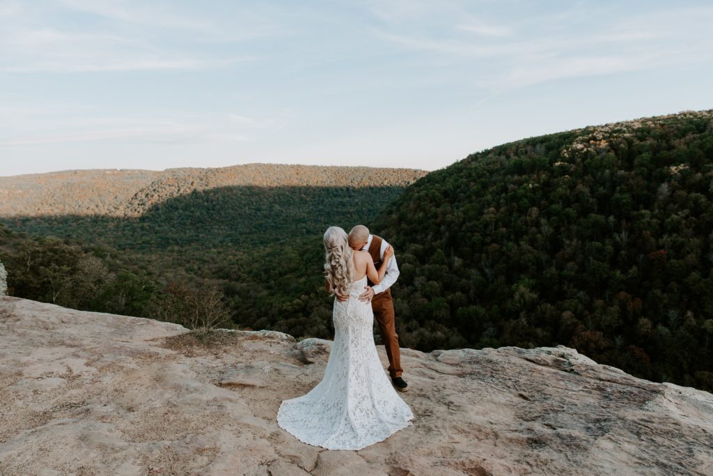A man kissing his partners neck with the mountains of the Ozarks in the background