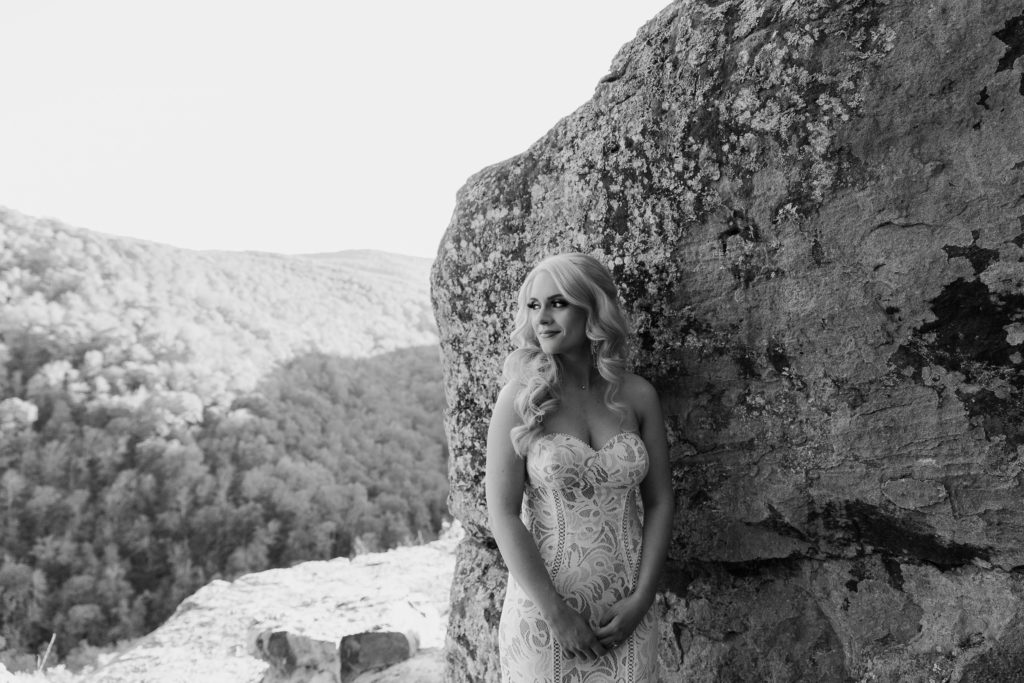 A bride leaning up against a rock looking off in to the distance during her hiking Arkansas elopement