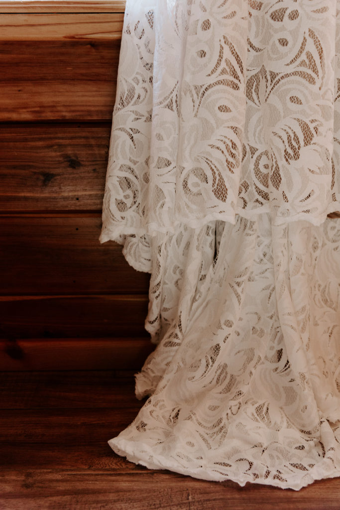 The lace of a wedding dress against the brown wood of a cabin during an all day elopement in the Ozarks