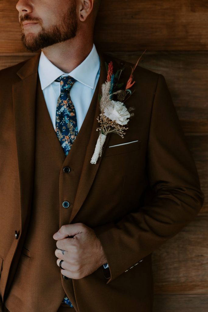 A close up of a man holding his suit jacket with a colorful fall boutonniere during groom portraits during his Ozarks elopement