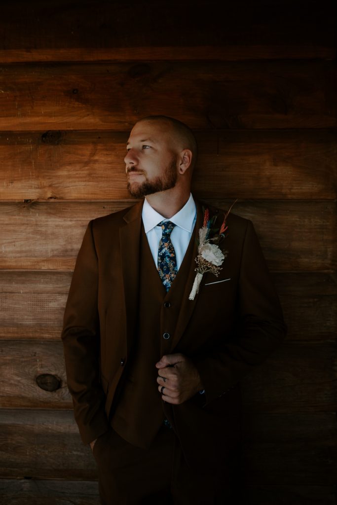A man holding his brown suit jacket looking off into the distance during his Ozarks adventurous elopement
