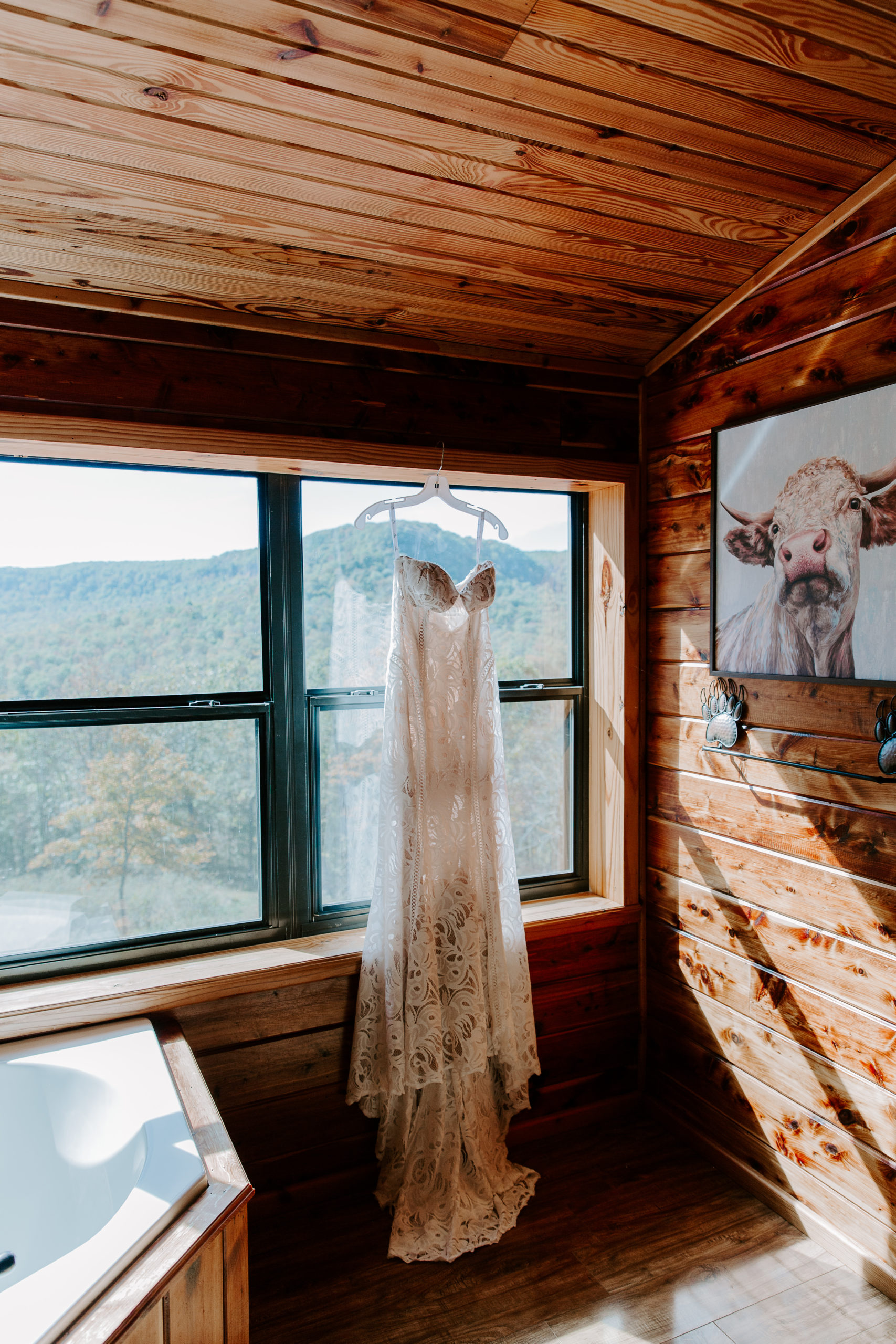 a lace wedding dress hanging in a window of a cabin on the side of the mountain in the Ozarks during an Arkansas elopement