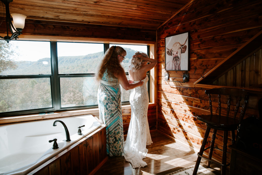 A mom helping her daughter into her wedding dress in the loft of a cabin during the daughters all day elopement