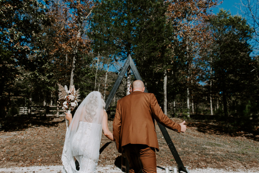 A man giving a thumbs up as he and his partner walk to stand in front of their elopement arch during their Ozarks intimate wedding