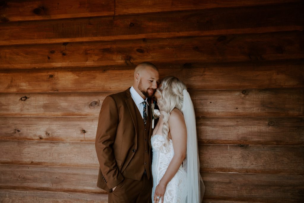 A woman kissing her partner on the cheek as they are standing in front of the cabin during their Arkansas elopement