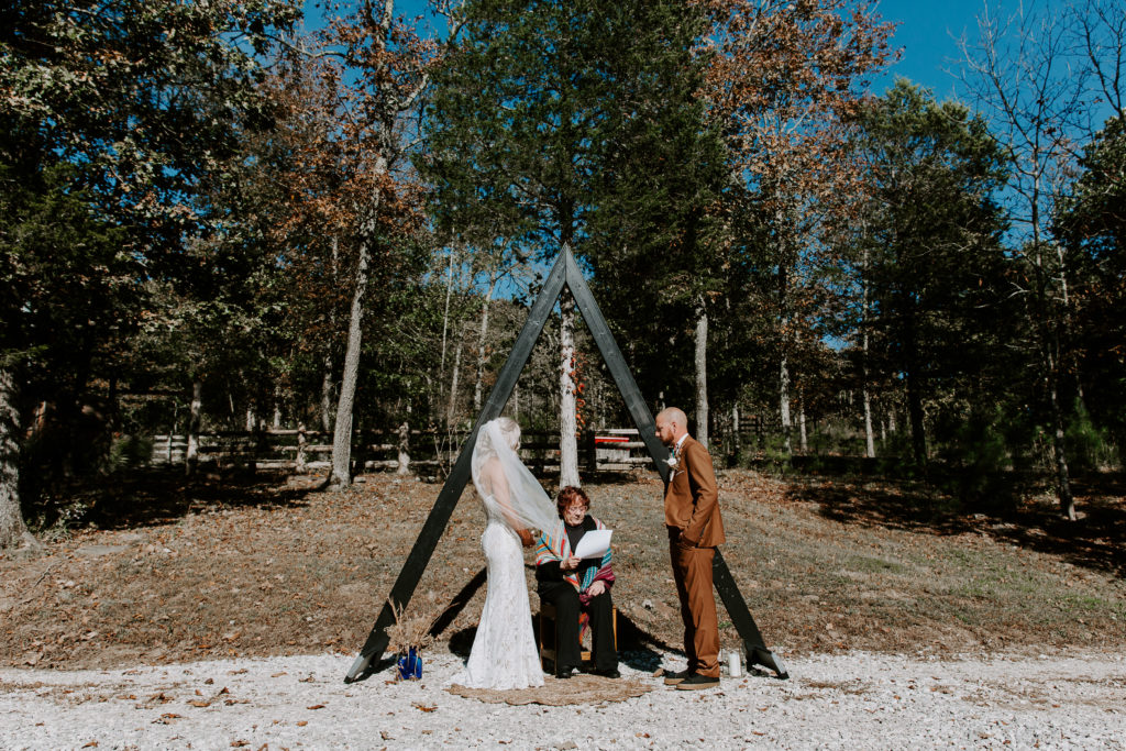 Couple standing in front of their ceremony arch with the officiant during their Arkansas elopement in the Ozarks