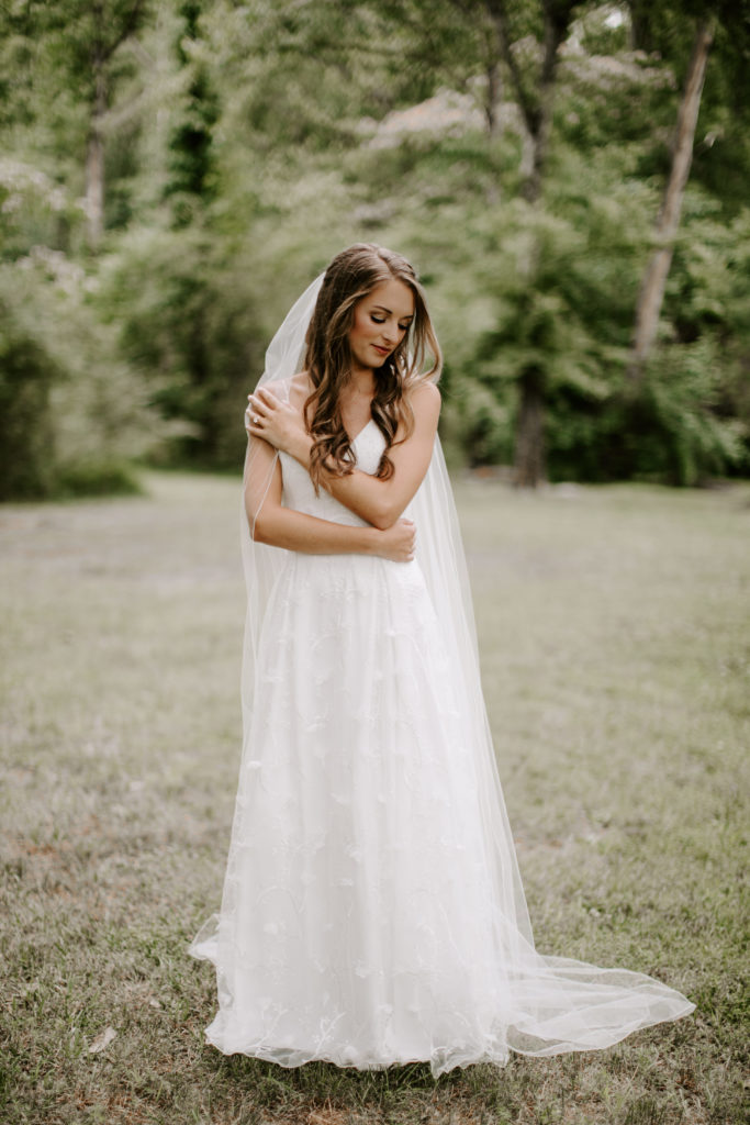 A bride holding her arms around herself as she looks down at the ground during her Tennessee summer wedding