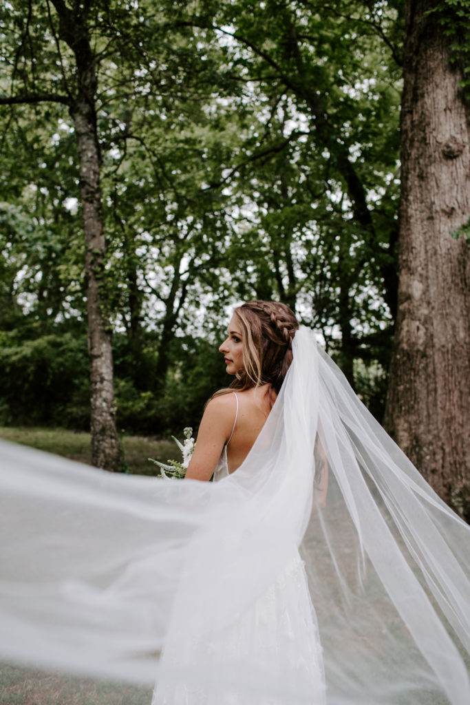 A woman standing with her back to the camera with her veil flowing out behind her as she looks off into the distance during her Knoxville wedding