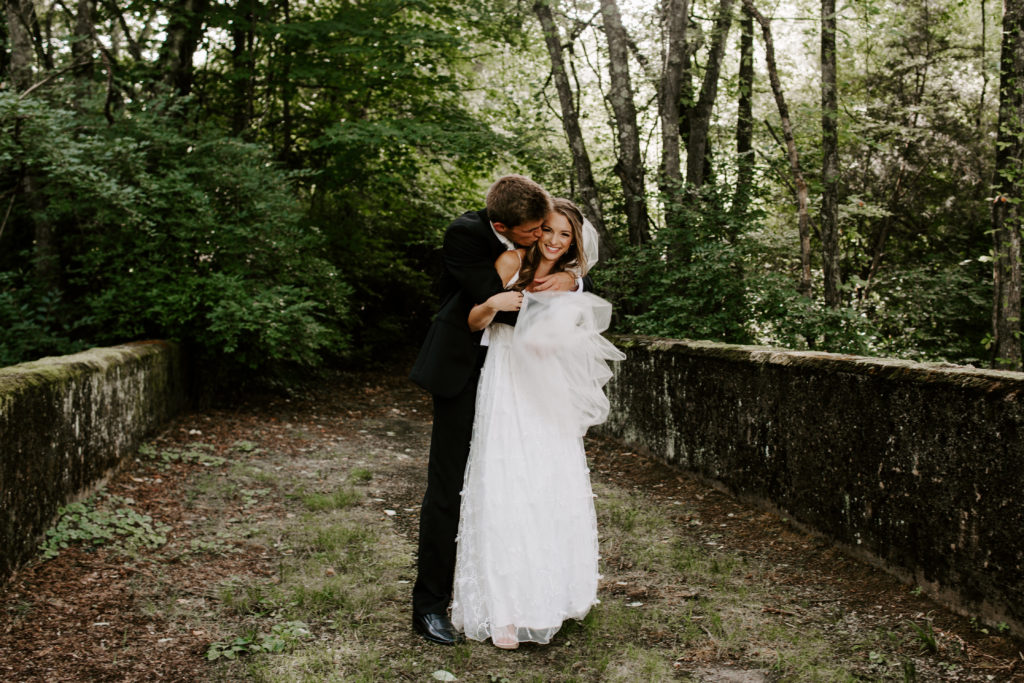 A man hugging his partner from behind while giving her a kiss on the cheek at the same time during their Tennessee wedding