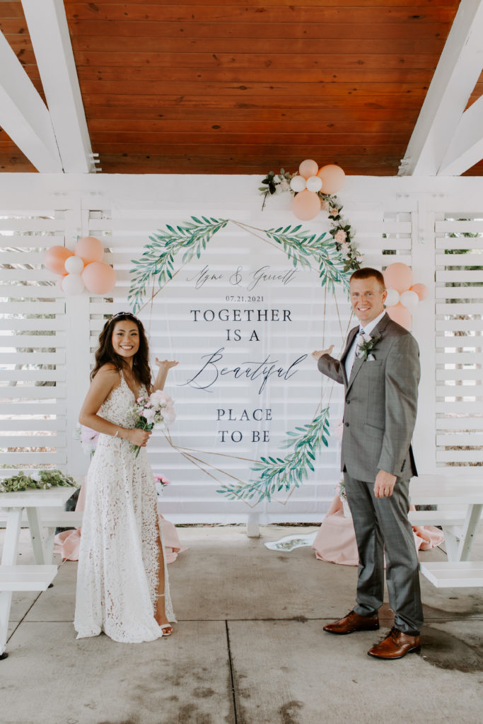 Couple standing on the sides of a banner that has their names and wedding date on it pointing towards it during their Florida intimate wedding