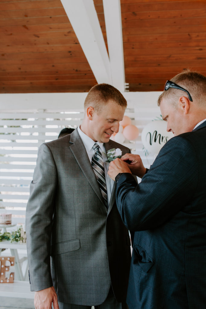 Groom's father pinning on boutonniere to his son before his parter is going to walk down the aisle