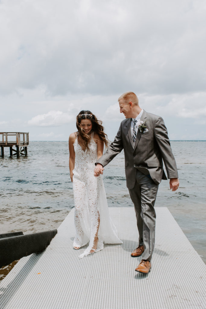 Couple holding hands and walking along a boardwalk with the ocean in the background as they are both laughing during their Florida destination wedding