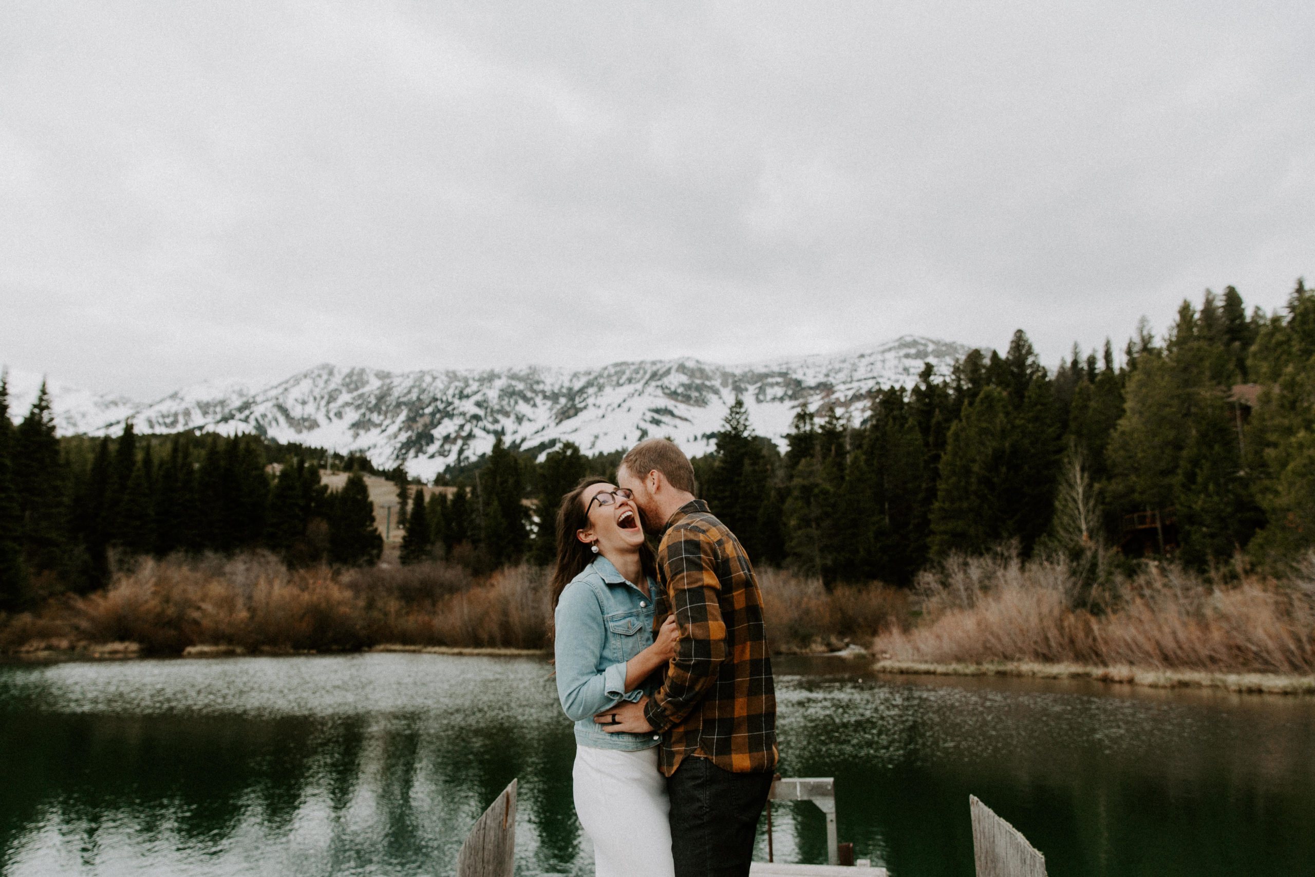 Man whispering into his partners ear as she laughs big with the mountains in the background during their Montana elopement