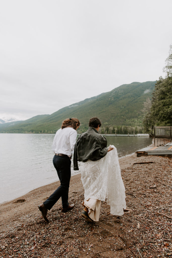 Newly wed couple holding hands and walking along the edge of a lake in Glacier National Park