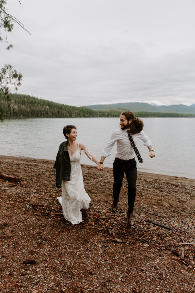 Couple holding hands and running away from the water during their mountain elopement in Montana