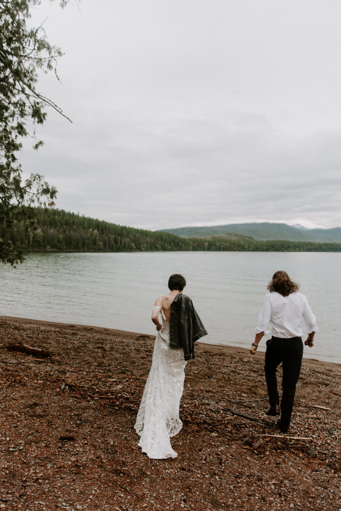 Woman holding a jacket over her shoulder as she and her partner walks towards the lake during their Montana elopement