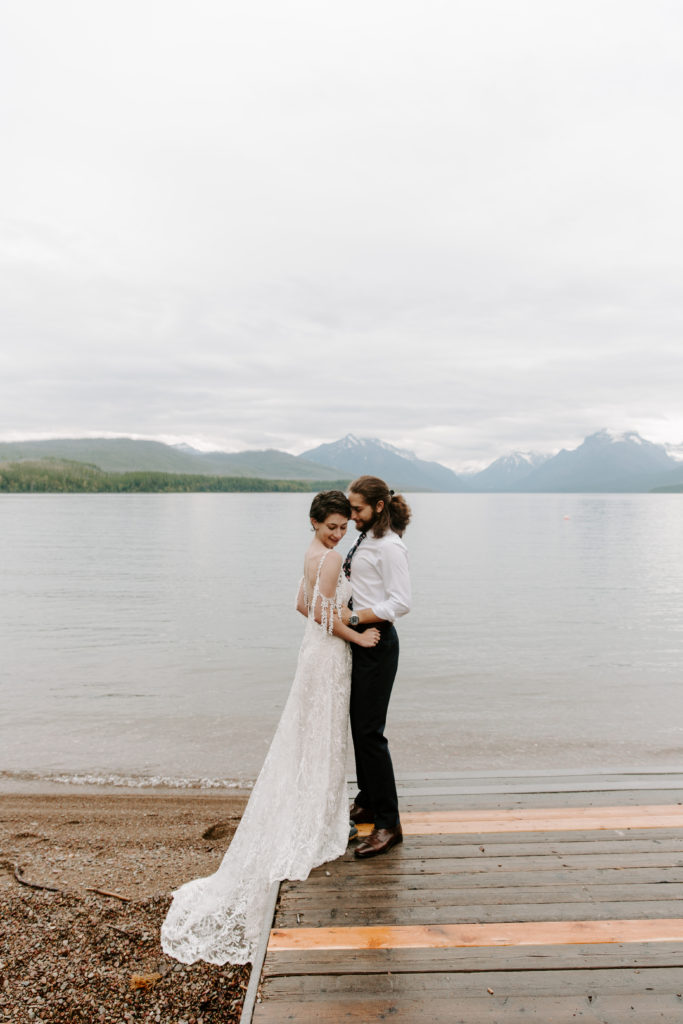 Couple standing on the edge of a dock as the man is nuzzling into his parters neck during their Glacier national park elopement