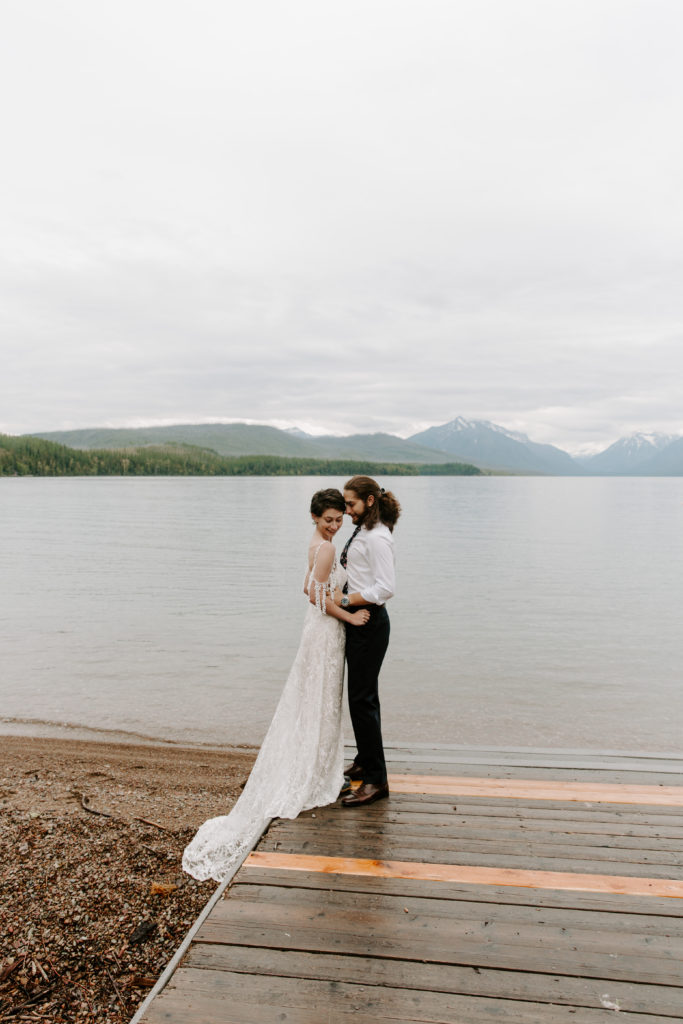Couple standing on the edge of a dock as the man is nuzzling into his parters neck during their mountain elopement
