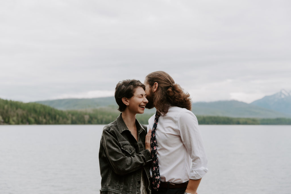 Man whispering into his partners ear as she is laughing with the mountains in the background during their Montana elopement
