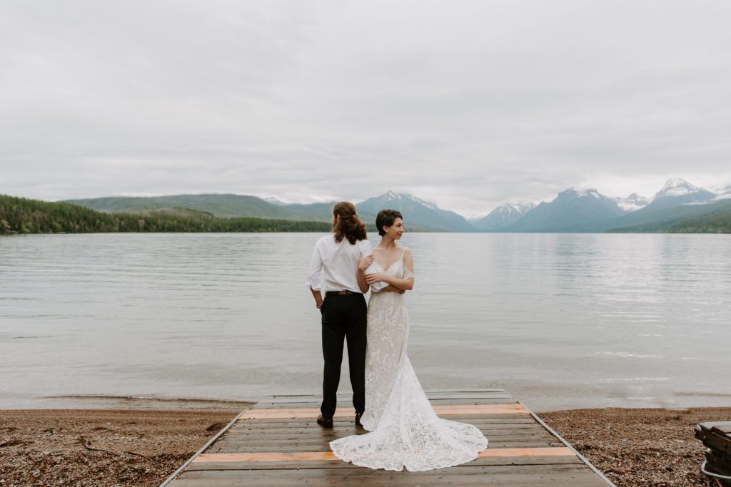 Man facing the lake with his partner holding onto his arm and facing away from him during their lake elopement in montana