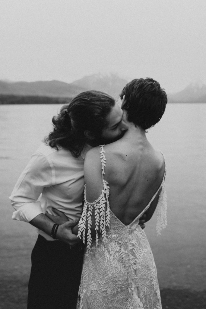 Man kissing his partners neck as they are holding hands with the mountains in the background during their national park elopement