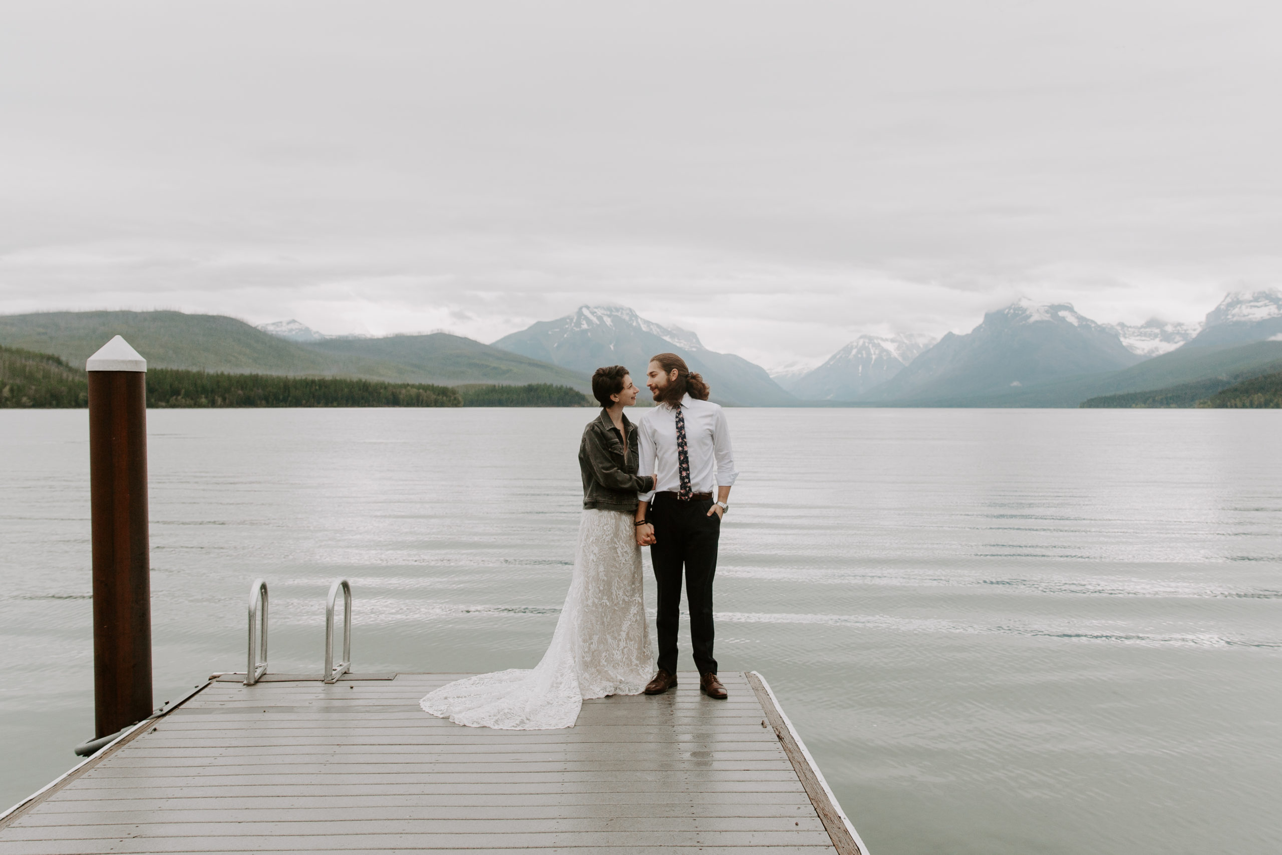 Couple standing on the end of a dock with the mountains during their sunrise elopement in Glacier National Park