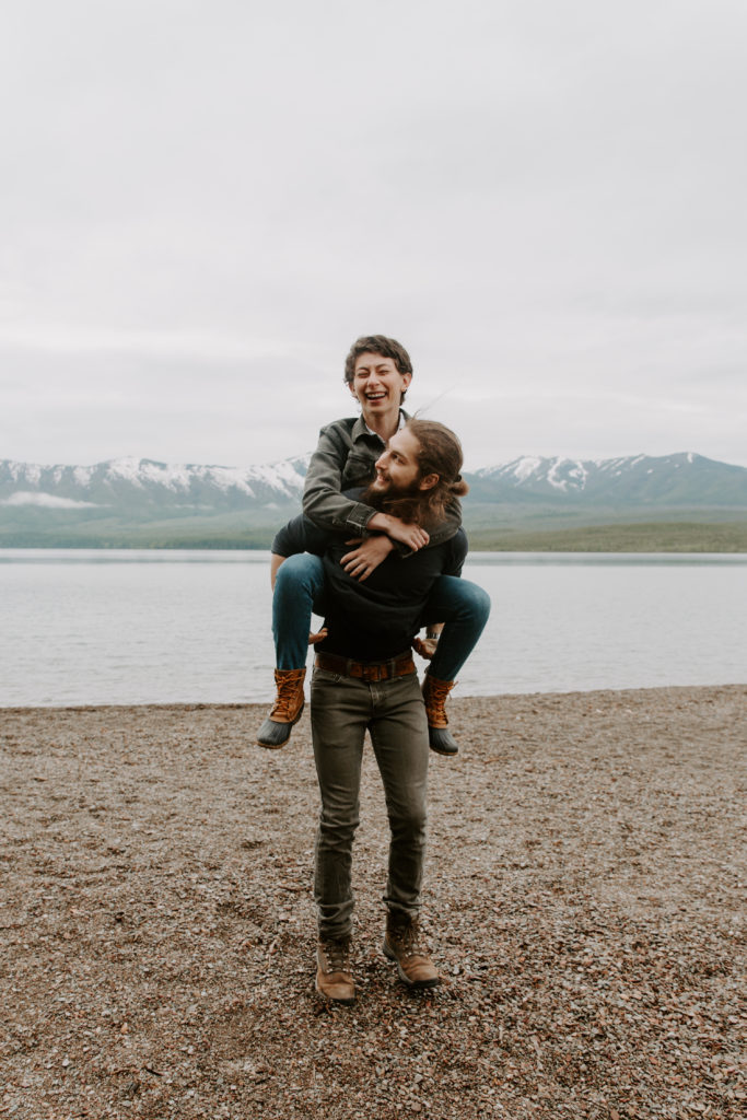 Man giving his partner a piggy back ride as she is laughing while exploring on their elopement day in glacier national park