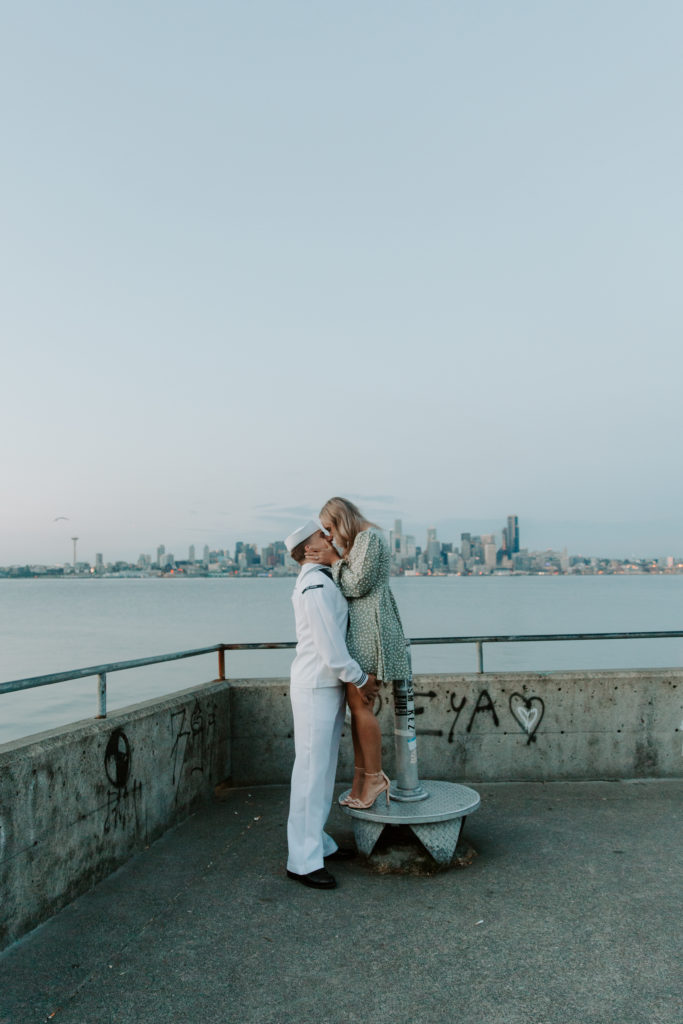 Woman standing on a view finder as her partner stands in front of her and they are sharing a kiss during their Seattle engagement photos in Washington