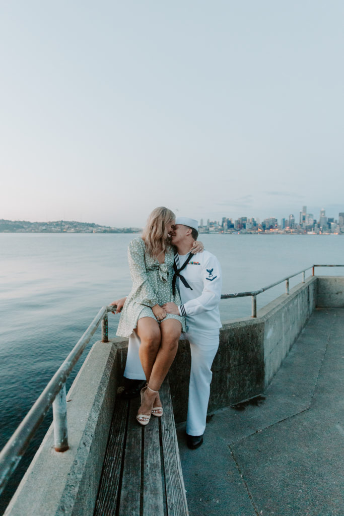 A woman sitting on her partners knee as they are leaning against the railing sharing a kiss during their Seattle Washington engagement photos