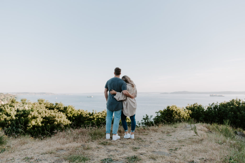 A couple looking off over Elliott Bay with their arms around each other during their Washington Engagement photos