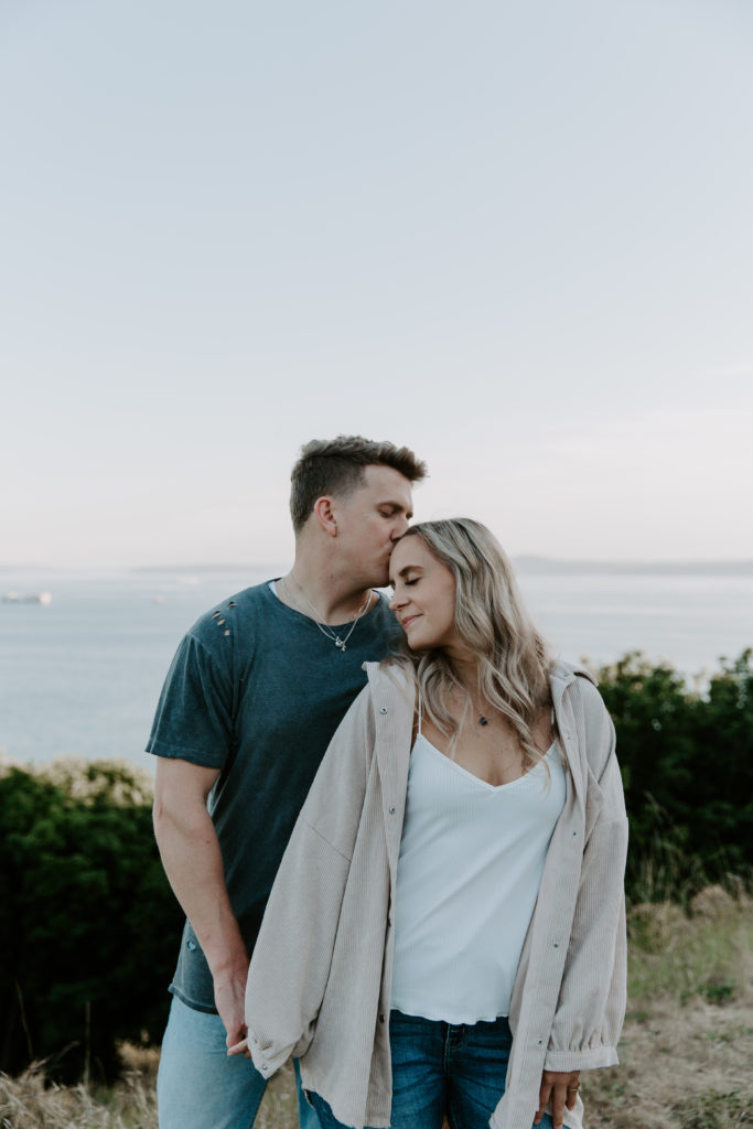 A man kissing his partner on the forehead as they are holding hands during their summer Seattle couple photos