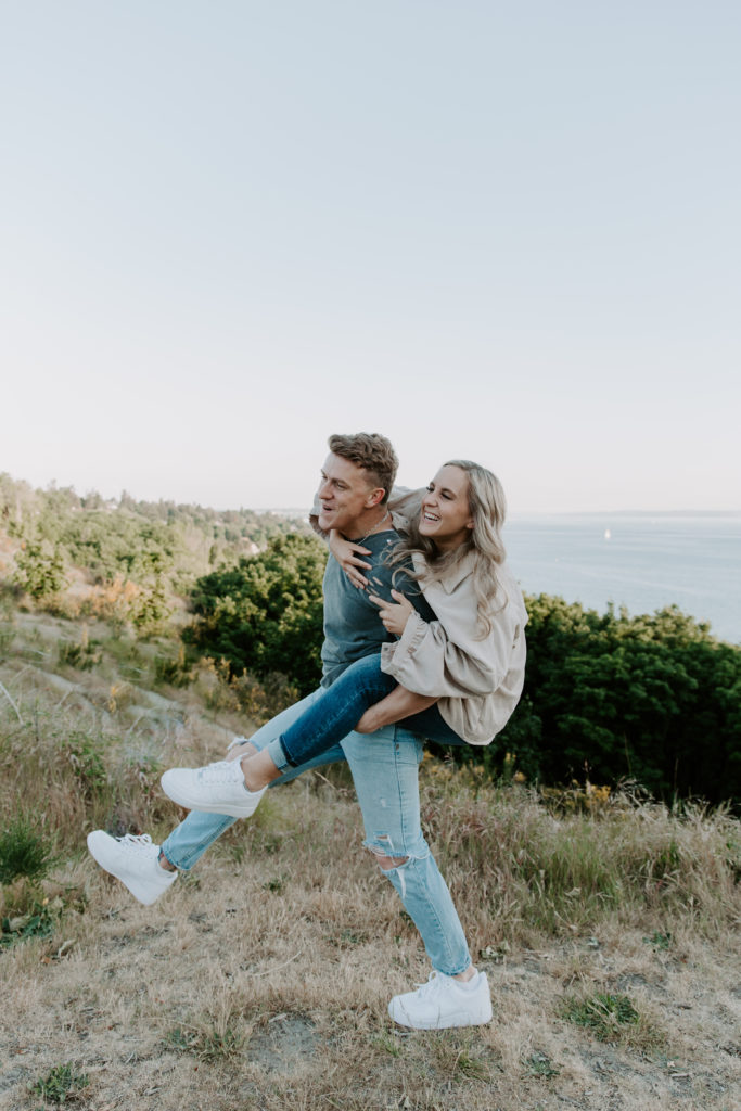 A man giving his partner a piggy back ride as they are walking up a hill during their Seattle Washington engagement photos
